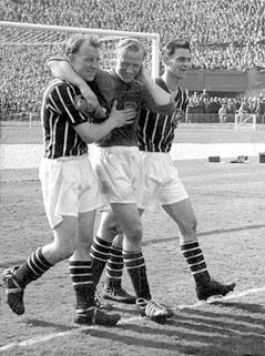 Bernd Trautmann greift sich nach dem FA-Cup-Finale 1956 auf seinen Nacken und wird von zwei Teamkollegen gestützt